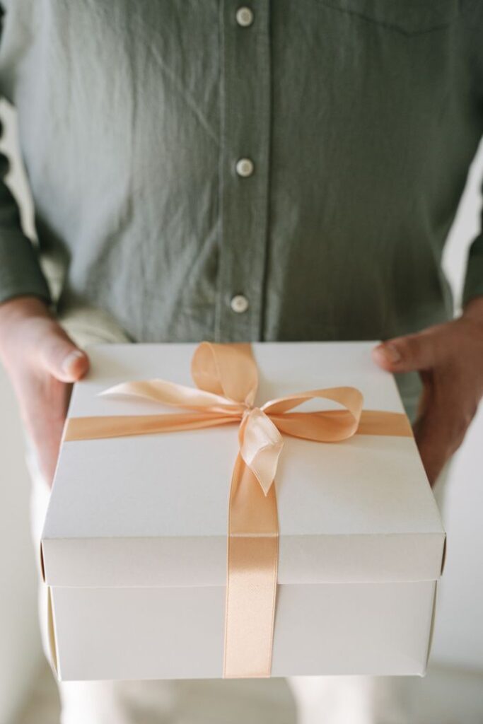 pexels-photo-7910657-7910657 A person holding a white gift box with a peach ribbon, perfect for celebrations.